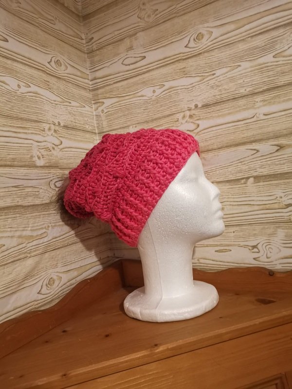 Rosa gehäkelte Beanie auf weißem Styroporkopf vor Holzpaneelwand