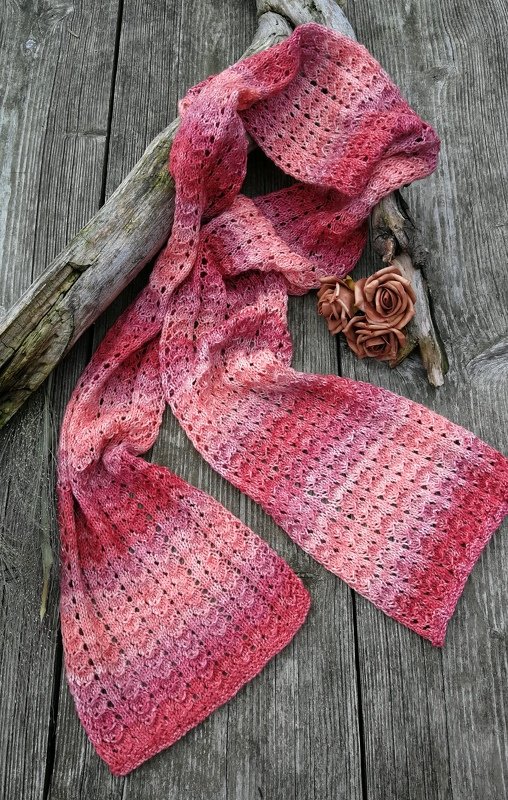 Rosa-roter Strickschal mit Ajourmuster auf rustikalem Holz, seitlich drapiert