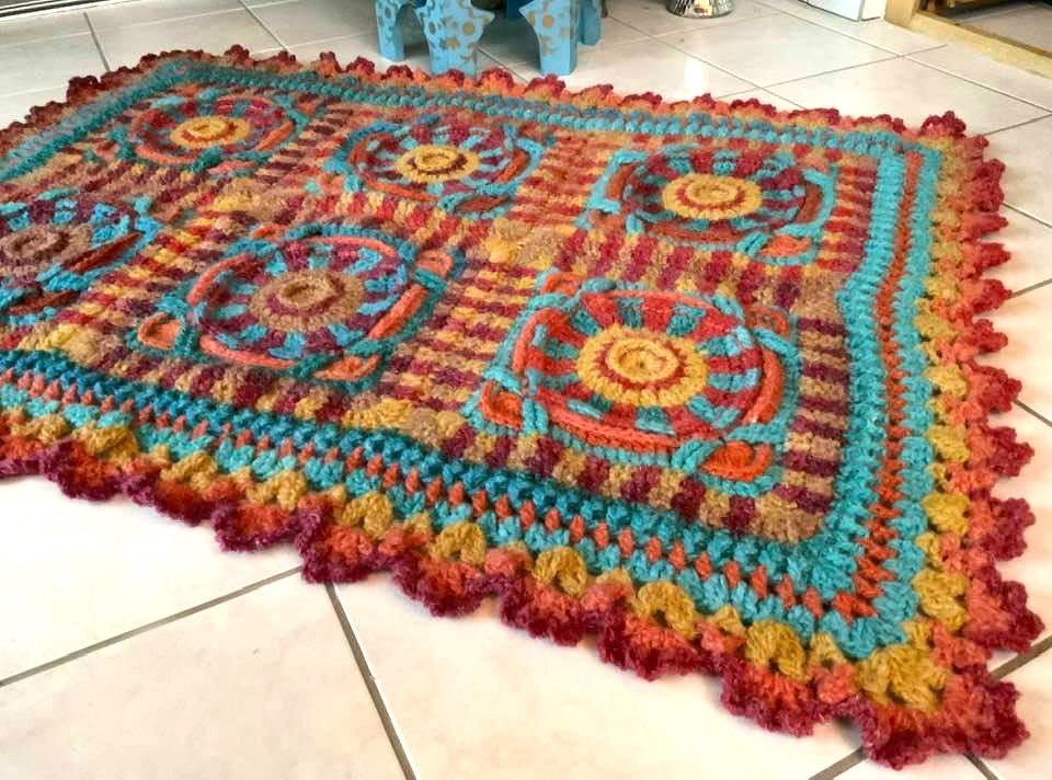 Bunte gehäkelte Decke mit runden Blumenmotiven und gewelltem Rand auf hellem Fliesenboden