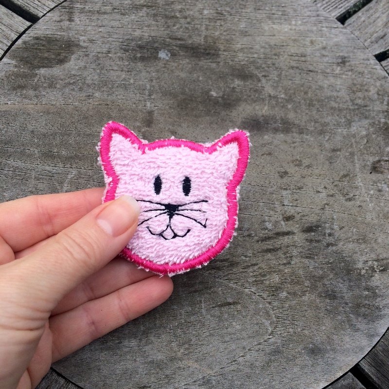 Rosa Katzengesicht als gesticktes Patch, in einer Hand gehalten auf Holzfläche