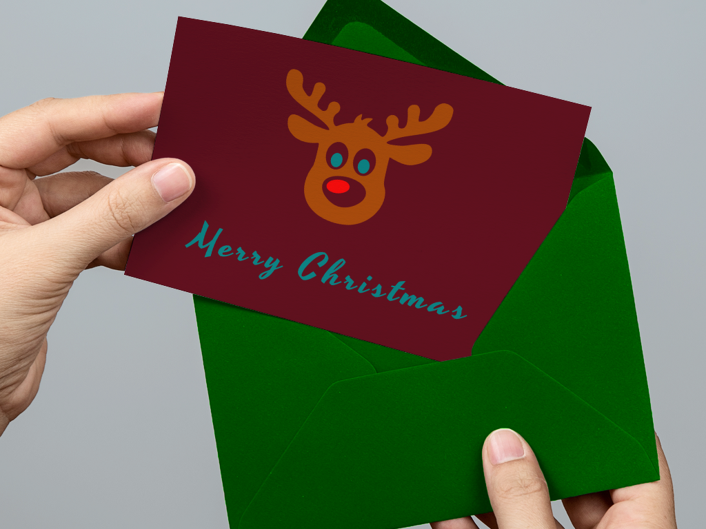 Hände halten grünen Umschlag mit burgunderfarbener Weihnachtskarte und stilisiertem Rentier