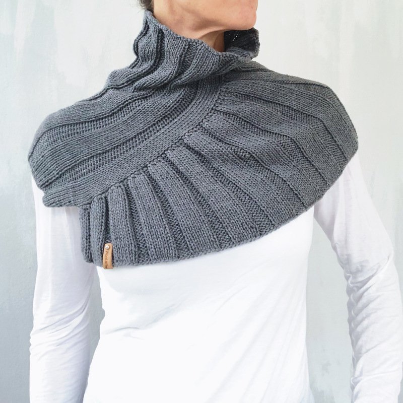 Person wearing a charcoal-gray ribbed knitted collar scarf with a rolled high neck over a white long-sleeve top