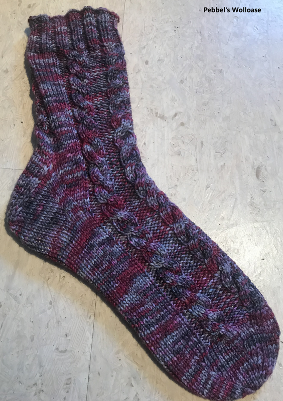 Gestrickte Socke mit Zopfmuster in Lila, Pink und Grau auf hellem Untergrund.