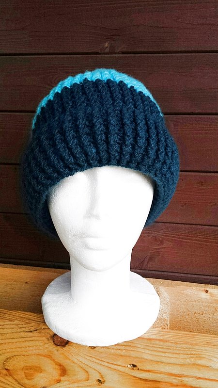 Gehäkelte Mütze in Dunkel- und Hellblau mit Rippenstruktur auf weißem Styroporkopf.
