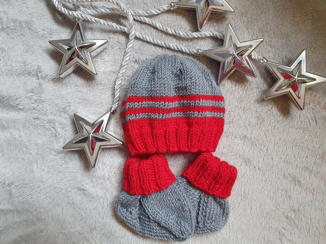 Gestrickte Babymütze und Babyschuhe in Grau und Rot auf flauschigem Untergrund mit silbernen Sternen