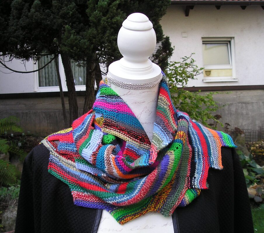 Bunt gestreiftes, handgestricktes Drachenschwanz-Tuch auf einer weißen Mannequin-Büste mit schwarzem Oberteil, im Freien drapiert.