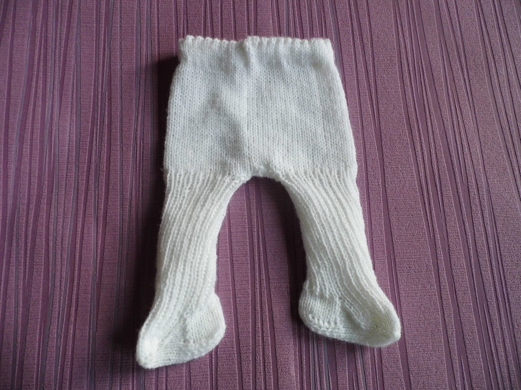 Weiße gestrickte Babystrumpfhose mit Füßchen auf violett gestreiftem Untergrund