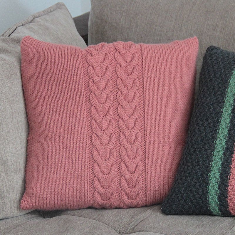 Quadratischer Kissenbezug in Rosé mit mittiger Zopfstruktur und glatt rechts gestrickten Flanken