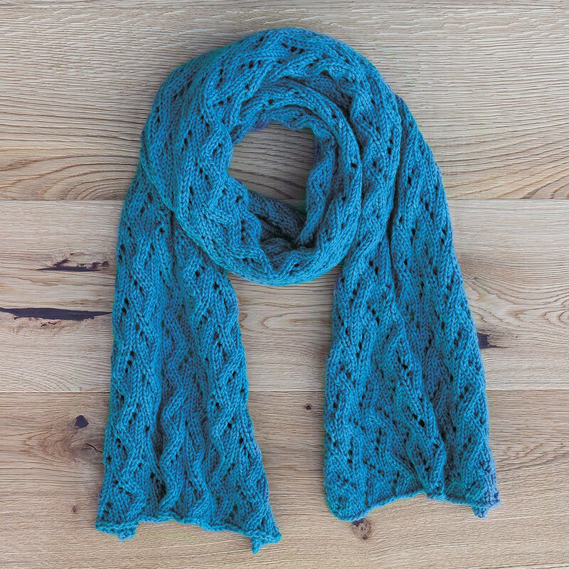 Türkisfarbener Strickschal mit filigranem Lochmuster auf Holz