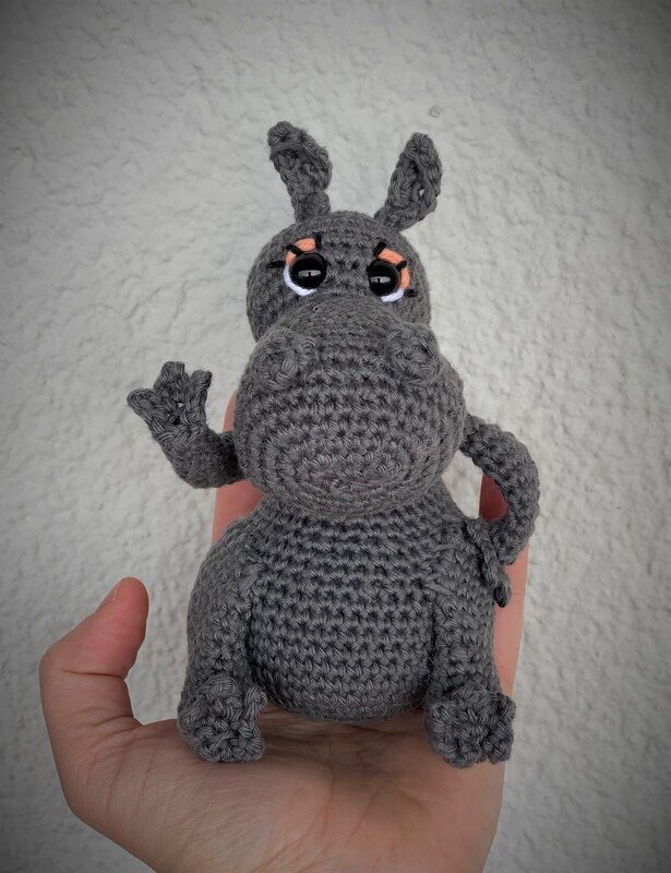 Gehäkeltes graues Nilpferd	Amigurumi in einer Hand, hebt einen Arm.