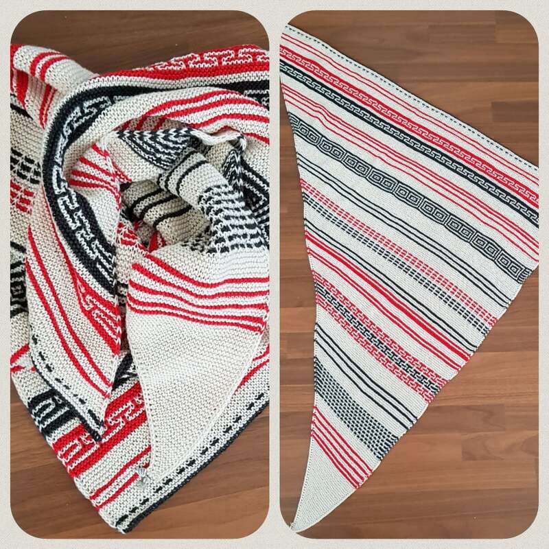 Gestricktes Dreieckstuch in Creme mit roten und schwarzen Streifen und geometrischen Borten, ausgebreitet auf Holzboden