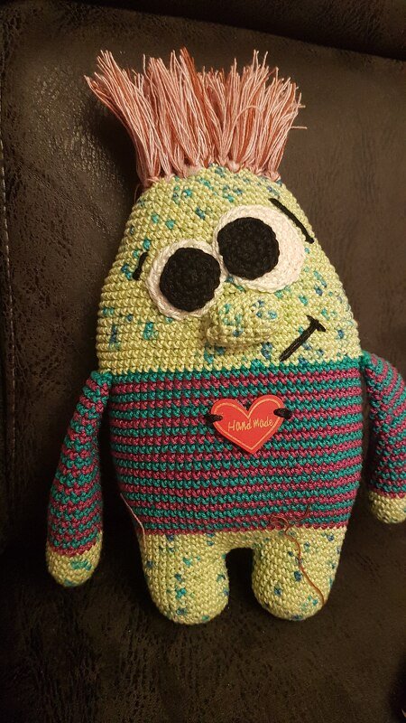 Gehäkeltes Amigurumi-Monster in Pastellgrün mit gestreiftem Torso, großen Augen und Fransenhaar