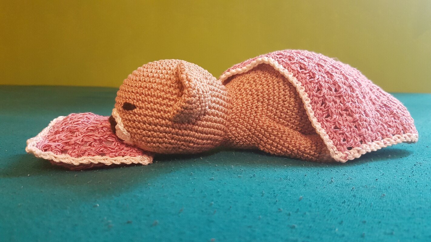 Gehäkeltes braunes Amigurumi-Schlafbärchen unter rosa Decke