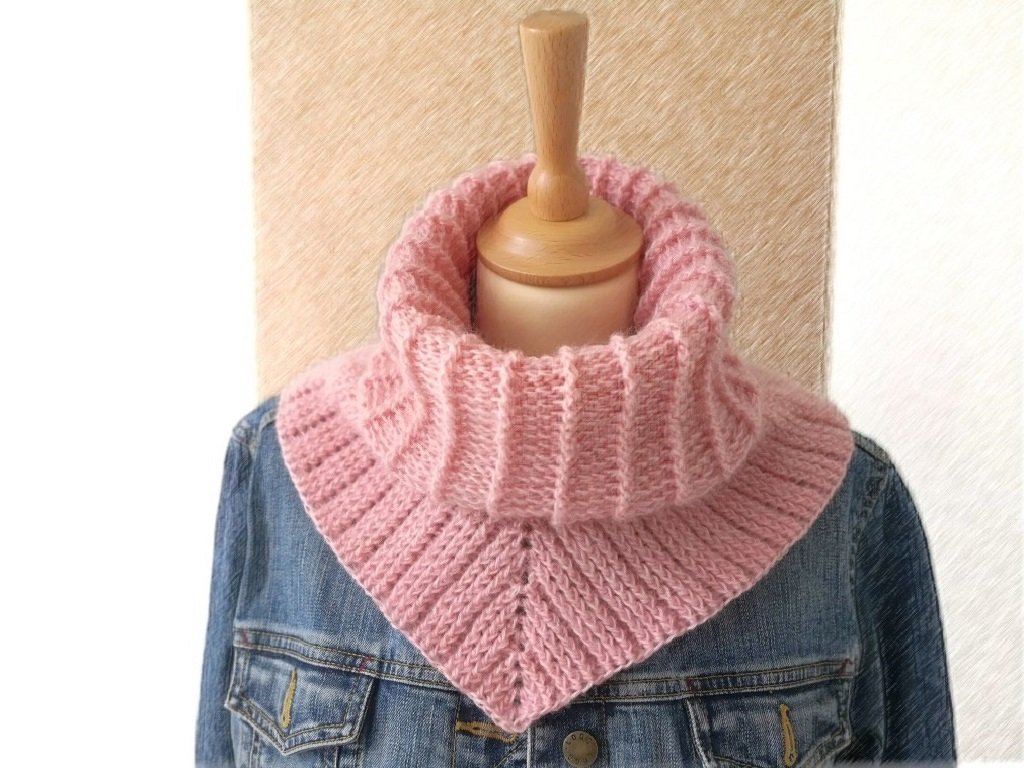 Rosa gehäkelter Kragenschal mit geripptem Kragen und dreieckigem Abschluss auf einer Schneiderpuppe über einer Jeansjacke.