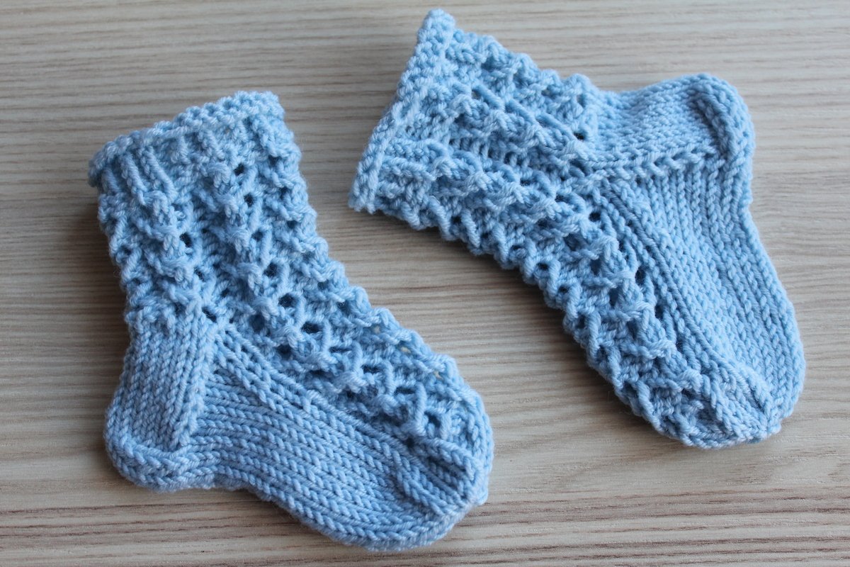 Hellblaue gestrickte Babysocken mit Ajourmuster auf hellem Holzuntergrund