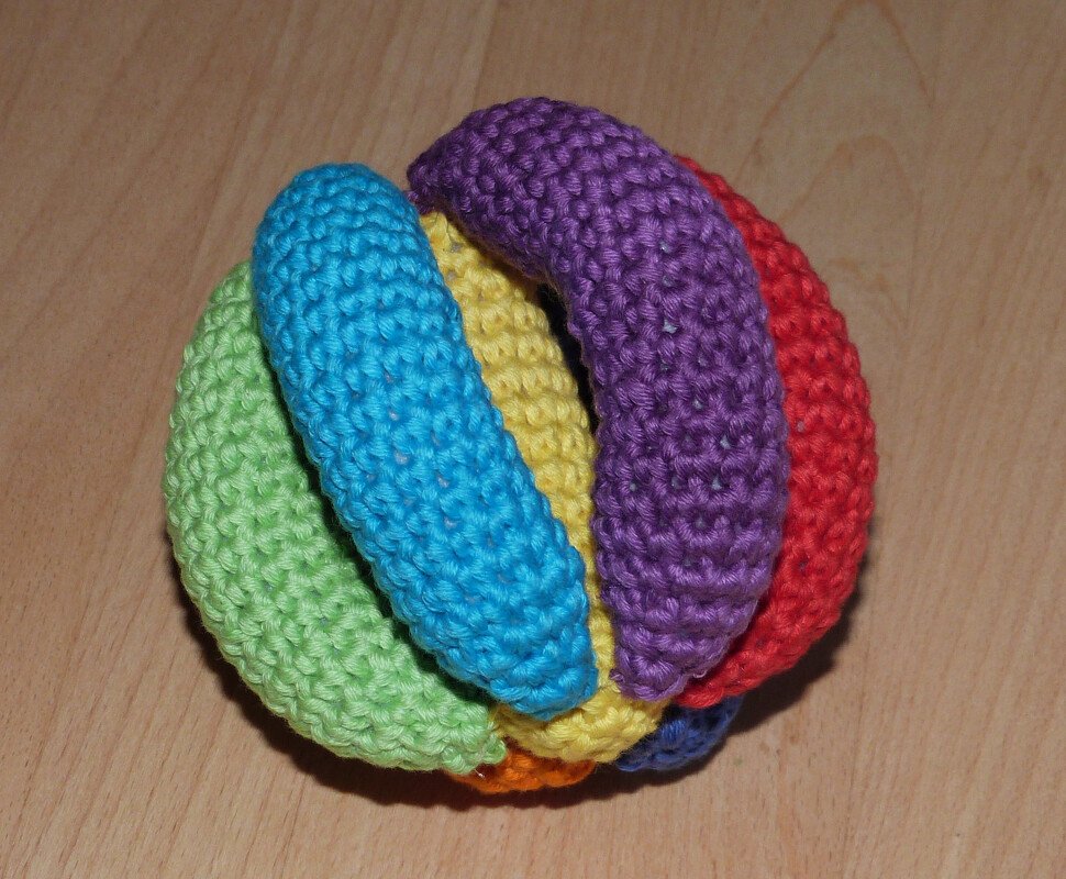 Gehäkelter bunter Greifball aus mehreren farbigen Segmenten auf Holzuntergrund