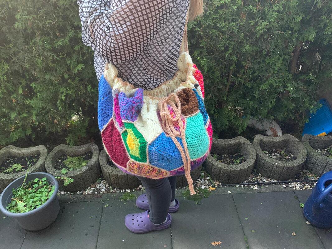 Bunte gehäkelte Umhängetasche im Patchwork-Stil mit Kordelzug an der Schulter getragen