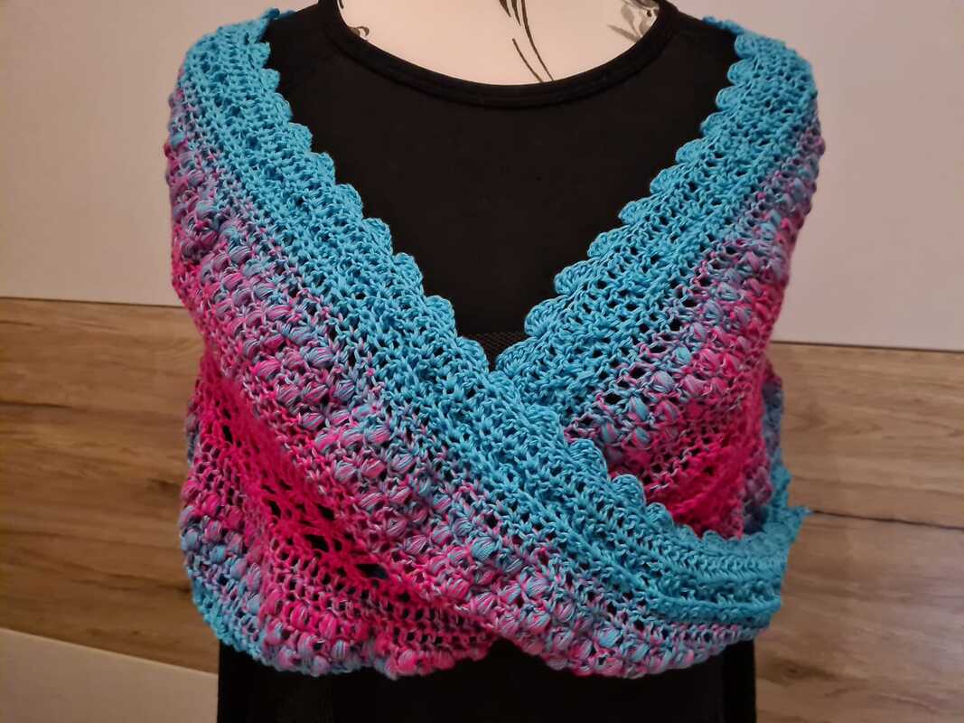 Gehäkelter Loop in Pink und Türkis mit Bobbelmuster und gewellter Kante, drapiert über eine schwarze Büste
