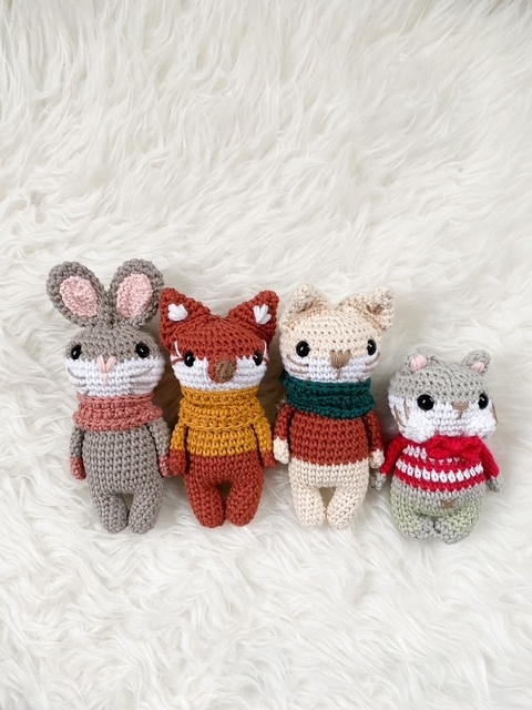 Vier gehäkelte Amigurumi-Greiflinge (Hase, Fuchs, Katze, Maus) auf weißem Kunstfell