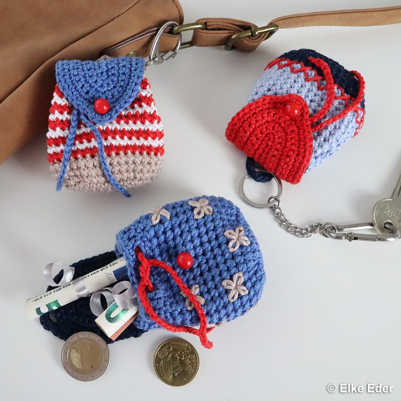 Three small crocheted backpack keychains: red-and-white stripe, blue-and-navy stripe, and blue with embroidered flowers.