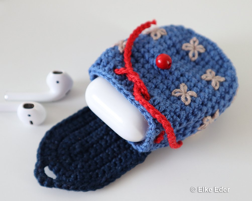 Compact blue crochet earbud cozy with red cord and bead closure beside white earbuds