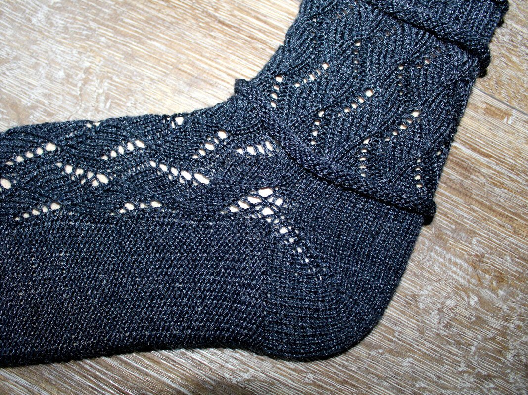Dunkelblaue Socke mit filigranem Ajourmuster auf Holzuntergrund