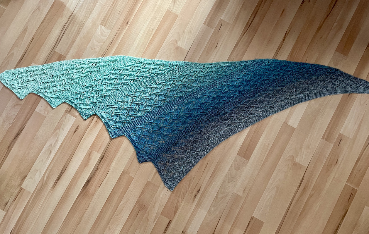 Gestricktes Dreieckstuch in Türkis bis Grau mit Lochmuster auf Holzfußboden