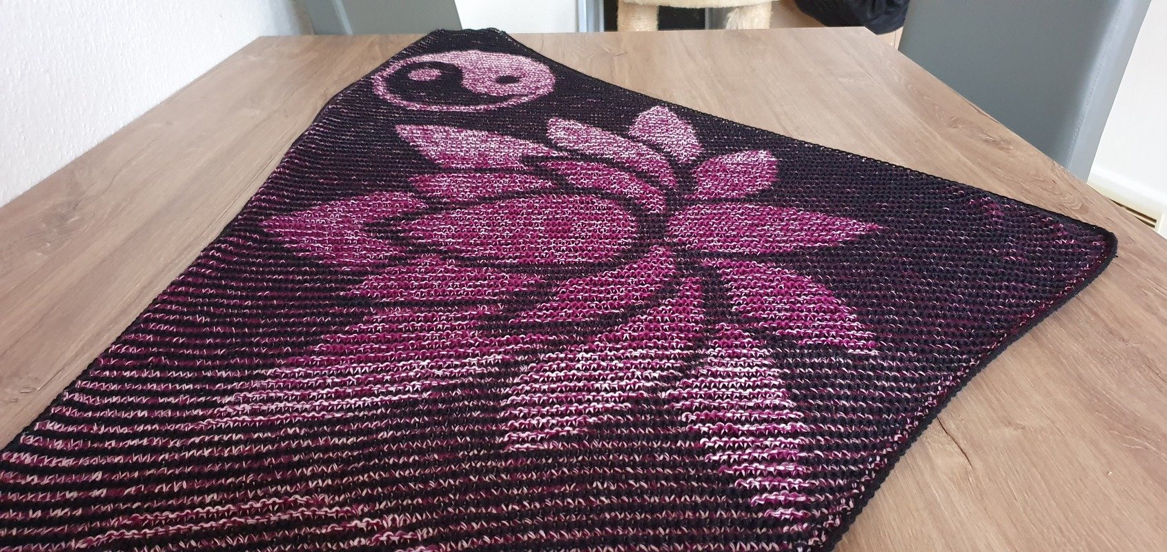 Triangular knitted shawl in dark and magenta tones featuring a large lotus motif and a Yin Yang symbol.