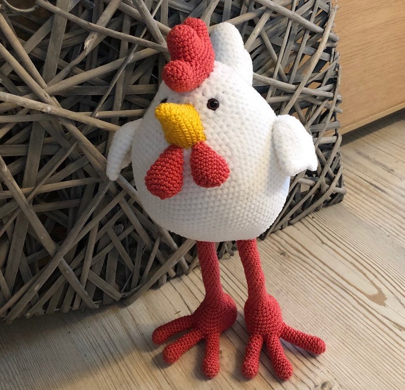 Weißes gehäkeltes Amigurumi-Huhn mit rotem Kamm, gelbem Schnabel und langen roten Beinen