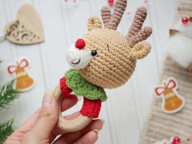 Hand holding a crochet reindeer baby rattle with wooden ring
