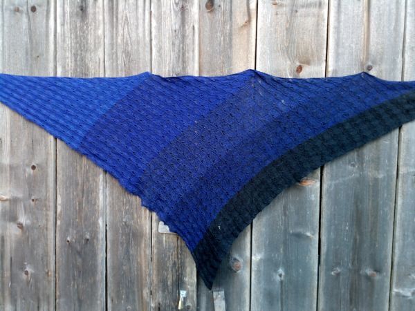 Gestricktes dreieckiges Tuch in Blau mit Lochmuster an Holzzaun