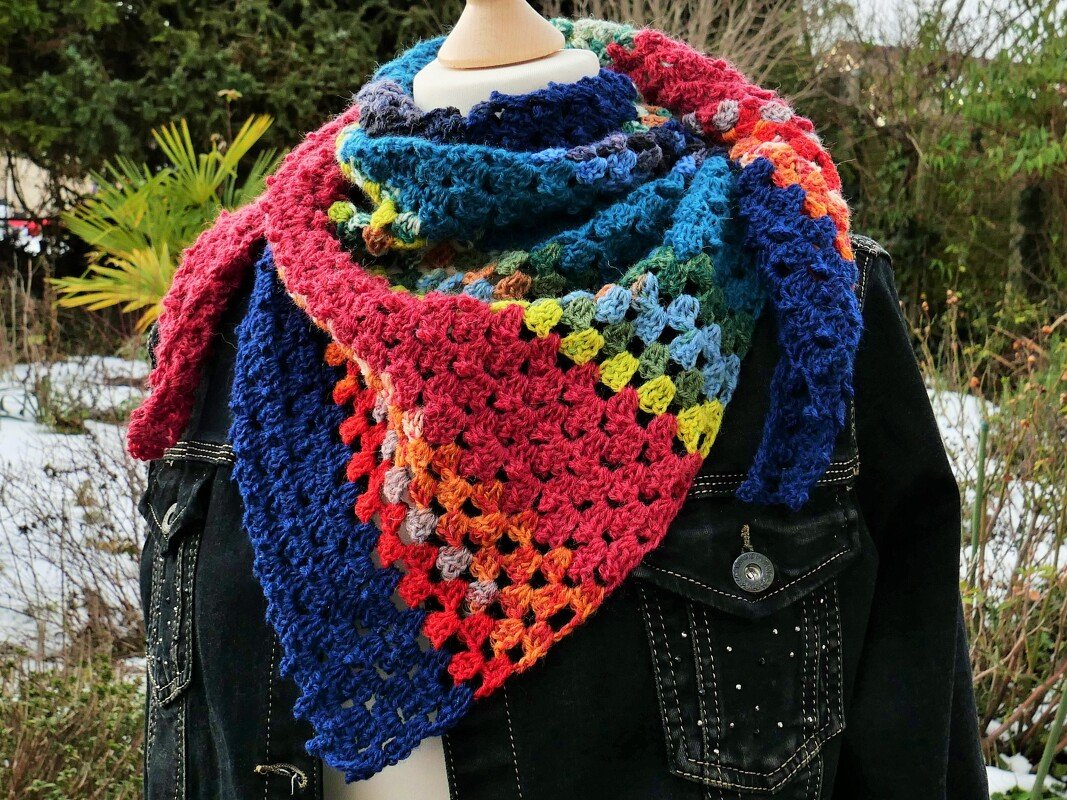 Buntes handgehäkeltes Dreieckstuch mit Granny-Square-Muster, über einer dunklen Jacke drapiert