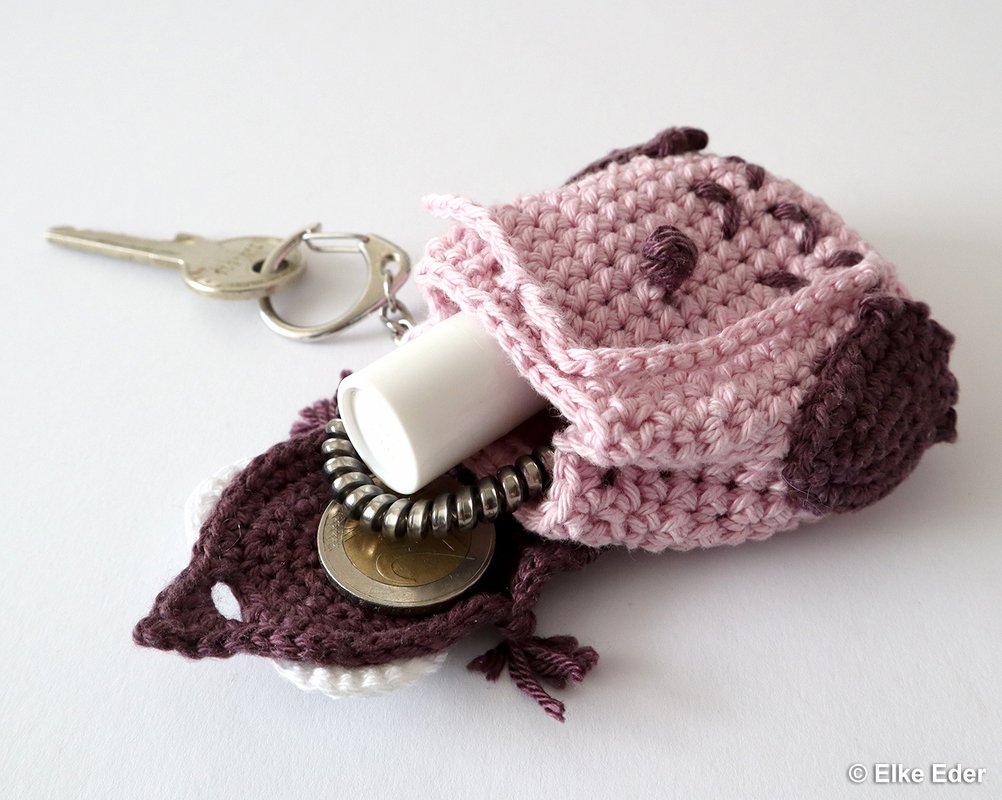 Compact pink crocheted key fob pouch holding a lip balm tube and coins, attached to a metal key ring