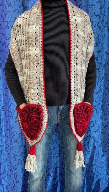 Langer gehäkelter Schal in Beige mit roten herzförmigen Eingrifftaschen und Quasten, über dunklem Pullover und Jeans getragen