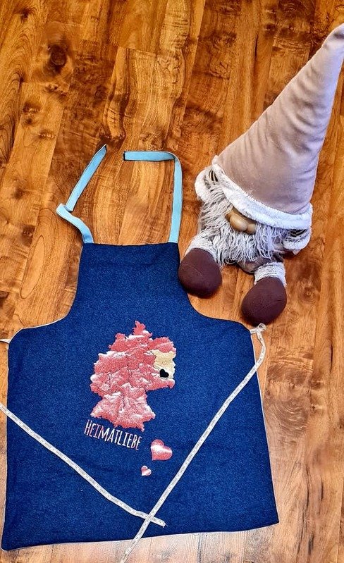 Dunkelblaue Schürze mit stilisierter Deutschlandkarte, Schriftzug „Heimatliebe“ und Wichtelfigur