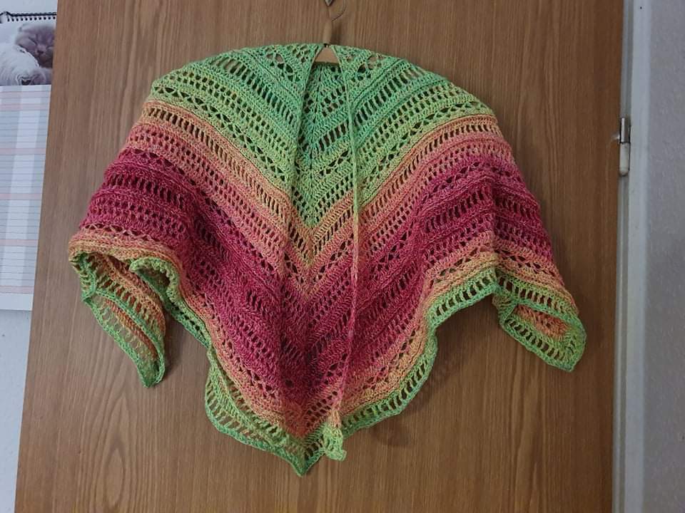 Gehäkeltes Dreieckstuch in Grün, Orange und Pink, an einer Holztür aufgehängt.
