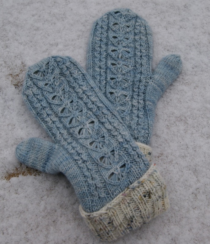 Hellblaue gestrickte Fäustlinge mit Loch- und Zopfmuster auf Schnee