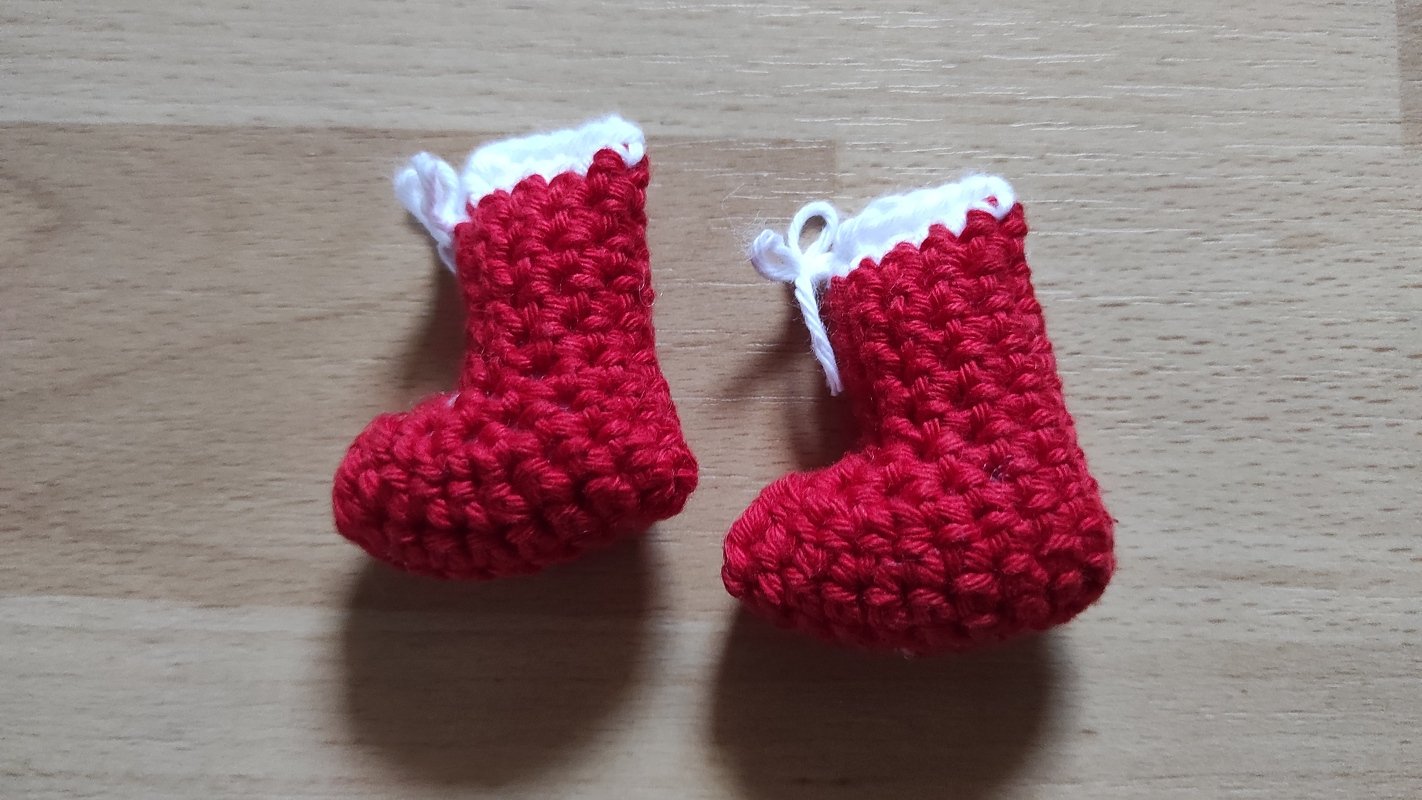 Zwei gehäkelte rote Weihnachtsstiefel mit weißem Rand auf heller Holzoberfläche