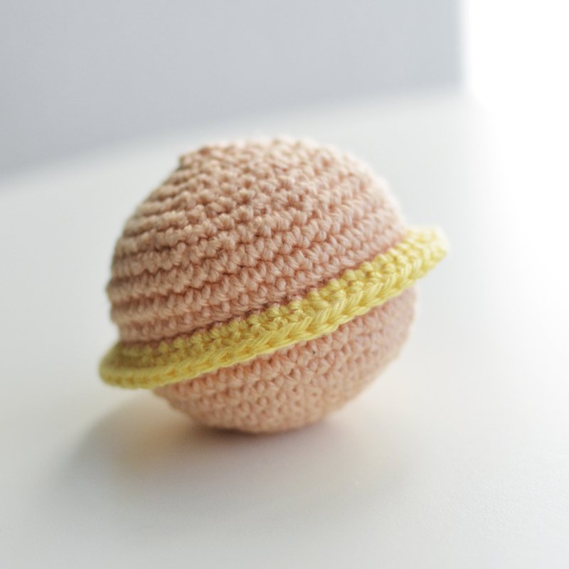 Nahaufnahme eines selbstgehäkelten Saturn-Balls in Beige mit gelbem Ring.