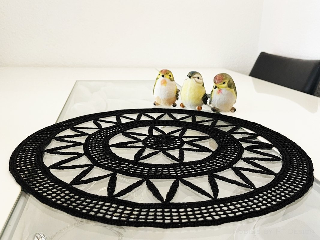 Black crocheted round doily with star pattern on a light table