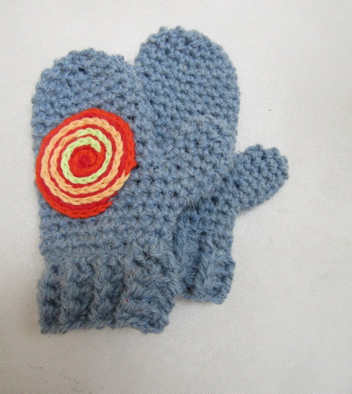 Hellblaue gehäkelte Kinderfäustlinge mit orange-gelber Spiral-Applikation