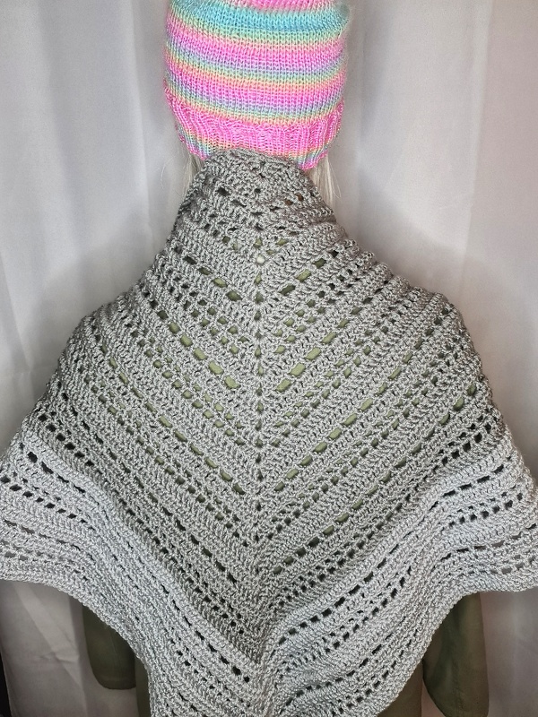 Rückansicht eines grauen gehäkelten Dreiecksschals mit Reihen aus Lochmuster und einer bunten Mütze