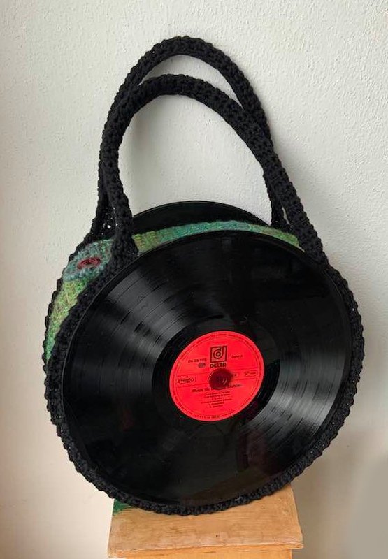Runde Handtasche mit schwarzen Schallplatten als Seiten, grün gehäkeltem Korpus und schwarzen Griffen.