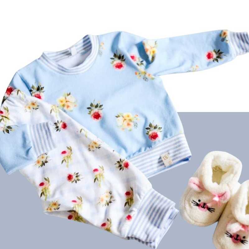 Babykleidung-Set: hellblaues Sweatshirt und weiße Hose mit Blumenmuster, dazu weiße Katzen-Hausschuhe
