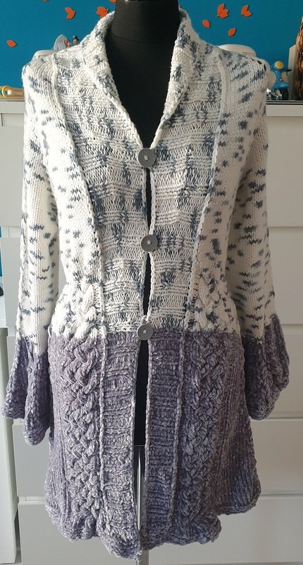 Lange zweifarbige Strickjacke in Cremeweiß und Lila-Grau mit Zopfmuster auf einer Schaufensterpuppe