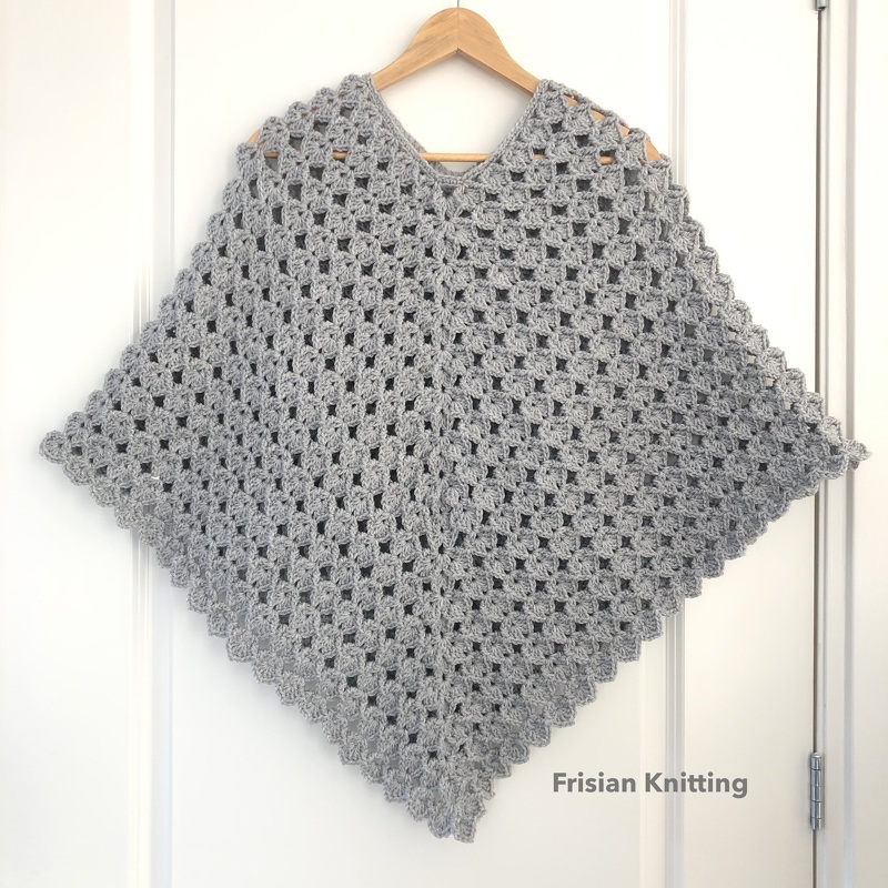 Grey crocheted V-neck poncho on wooden hanger with diamond shape and scalloped edge