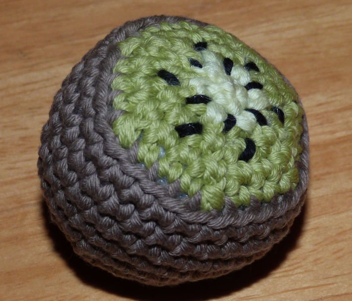 Nahaufnahme einer handgehäkelten Kiwi mit brauner Schale und grünem Fruchtfleisch