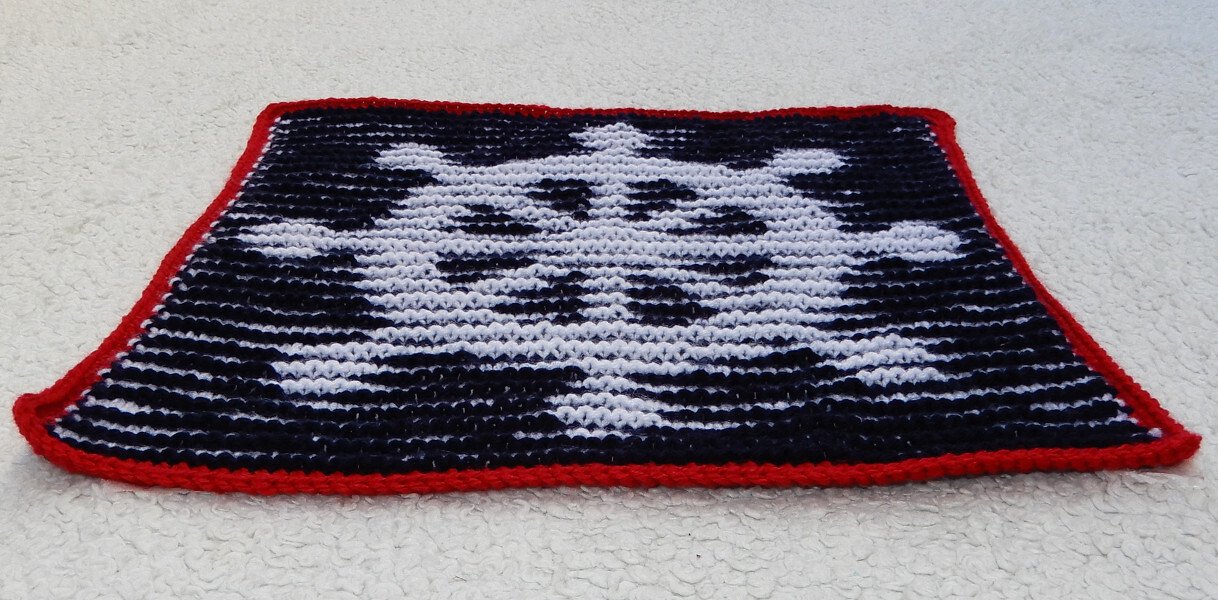 Gestricktes rechteckiges Panel mit weißem Totenkopf auf schwarzem Hintergrund und rotem Rand