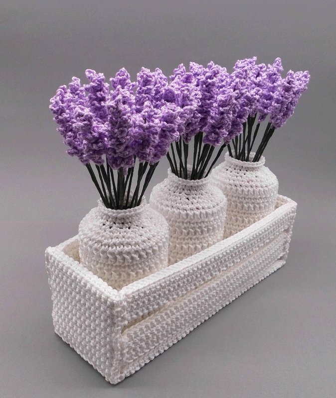 Three purple crocheted lavender stems in white crocheted vases inside a rectangular crocheted tray