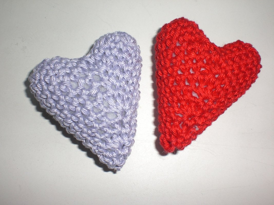 Zwei gehäkelte Herzen, rot und lavendelfarben, auf hellem Untergrund.